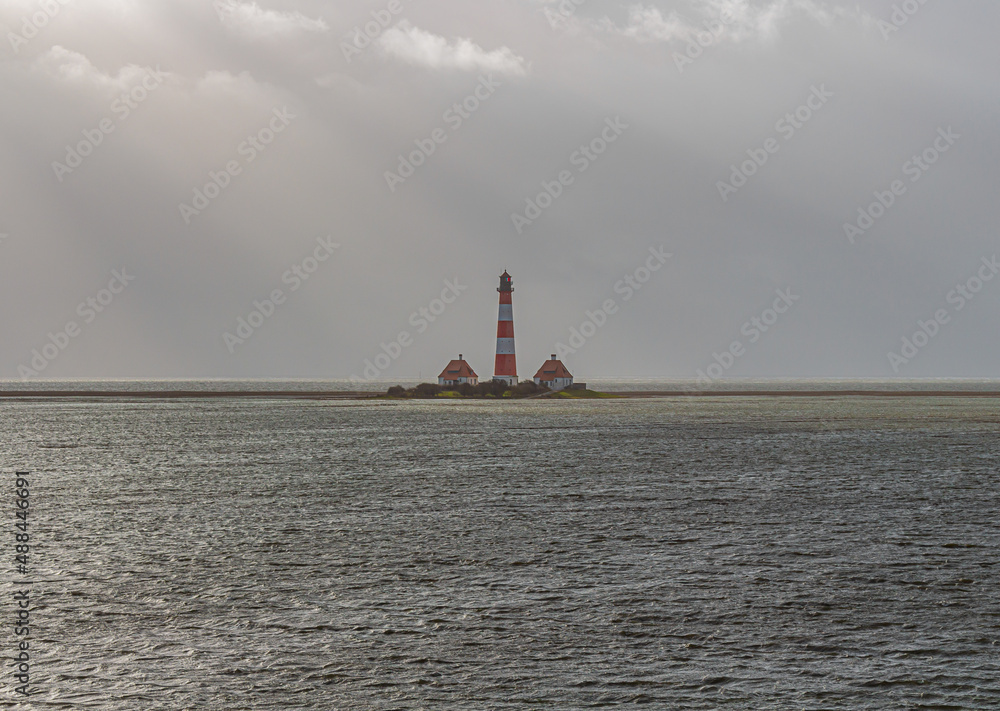 Der große Leuchtturm von Westerhever steht nach einer Sturmflut bei schönem Wetter und Sonne mitten in den Wellen der Nordsee.