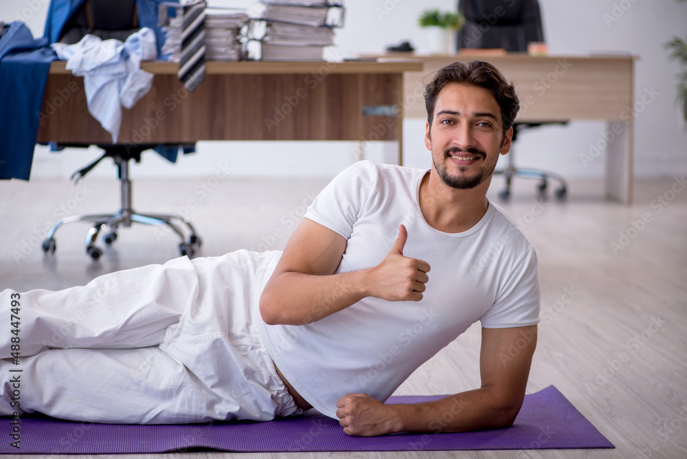 Fototapeta premium Young male employee doing sport exercises in the office