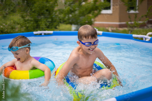 Two boys brothers in the outdoor outdoor pool near the house swim and play. Colored, swimming, bright, rainbow circles.