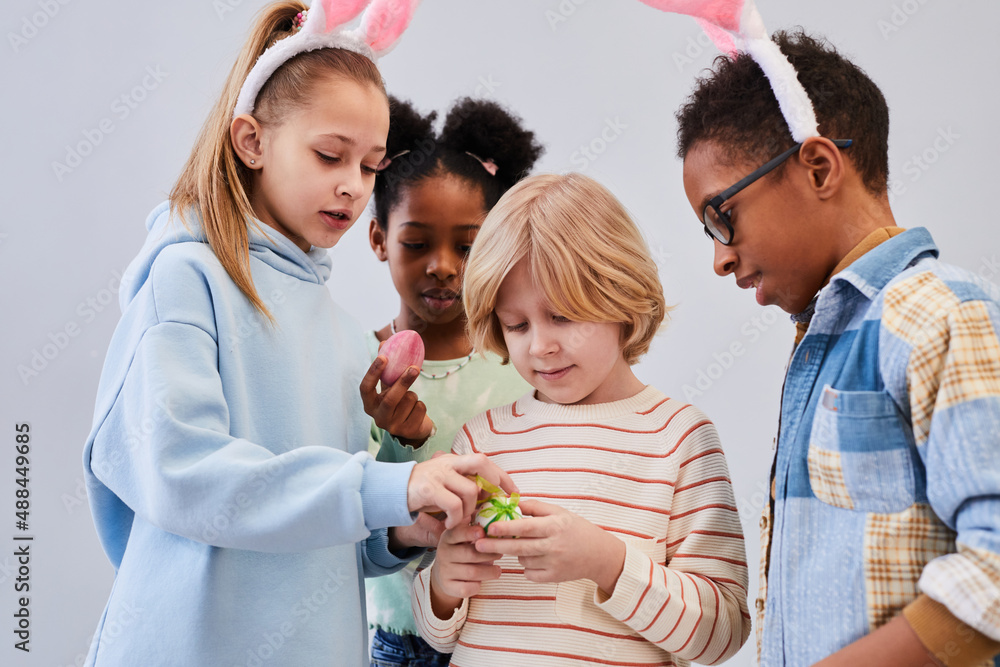 Diverse group of children wearing bunny ears and playing with Easter eggs against white background Diverse group of children wearing bunny ears and playing with Easter eggs against white background
