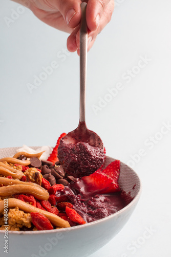 acai bowl spoon, with bananas, granola, strawberries, almonds, blue background