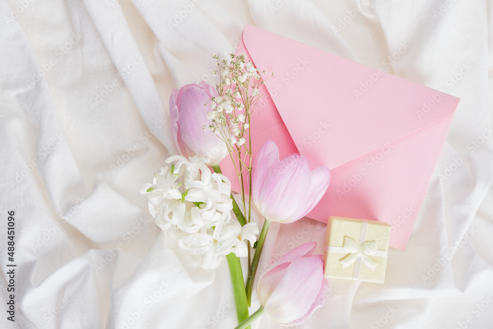 a bouquet of spring flowers in delicate shades, a small yellow gift box and a pink envelope on the bed a bouquet of spring flowers in delicate shades, a small yellow gift box and a pink envelope on the bed