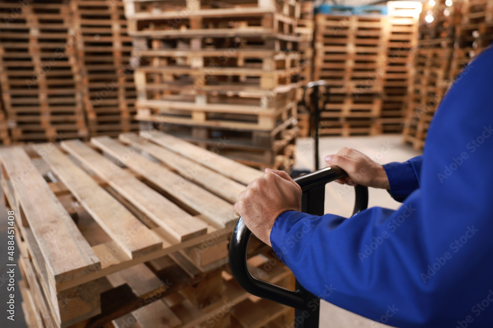 Worker moving wooden pallets with manual forklift in warehouse, closeup - obrazy, fototapety, plakaty 