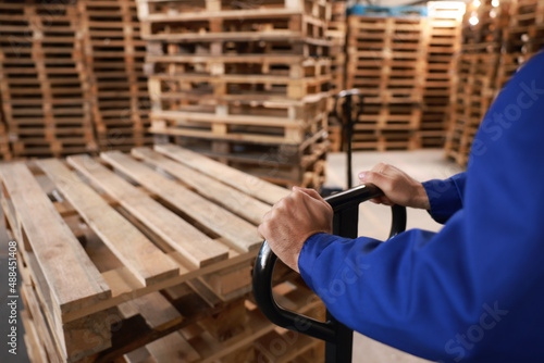 Worker moving wooden pallets with manual forklift in warehouse, closeup photo