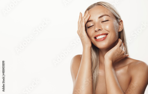 Beauty and skincare. Beautiful female model cleaning her face with cosmetic product, cleansing gel and smiling, touching facial, standing with naked shoulders against white background