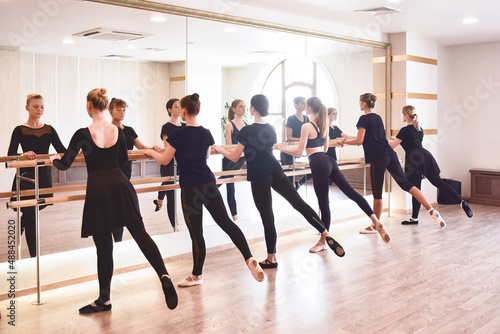 Group of people doing exercises using barre in gym with focus to fit athletic toned .woman in foreground in health and fitness concept.