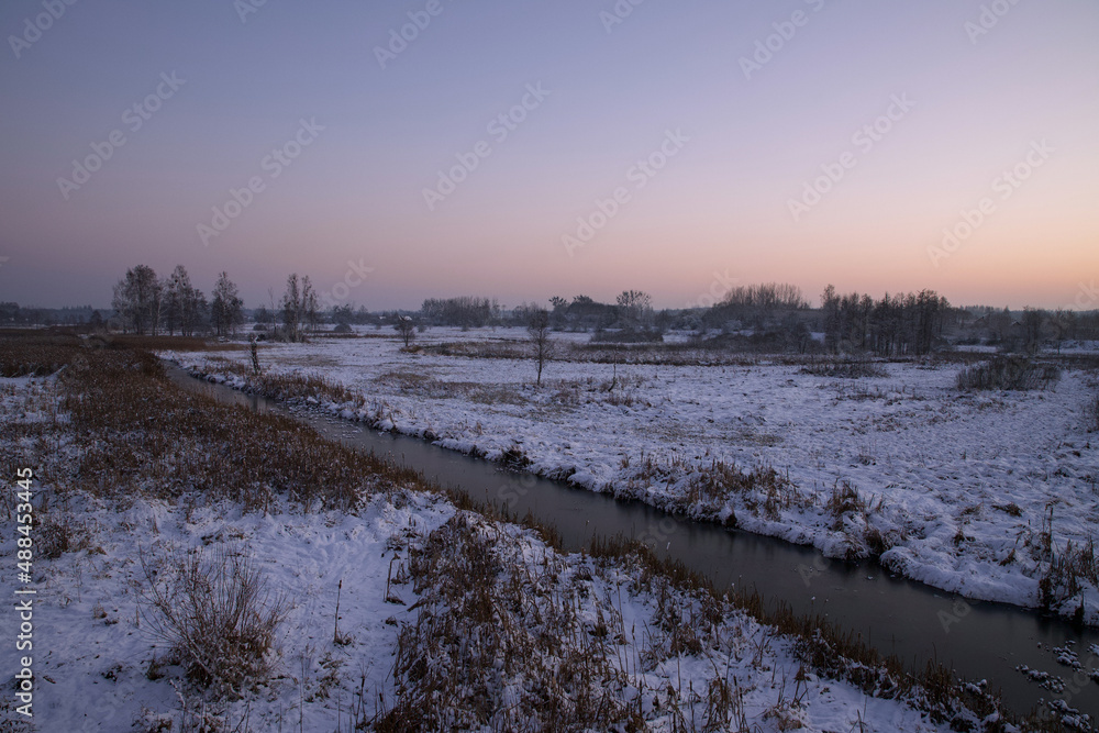 Winter landscape with a river at sunset time.