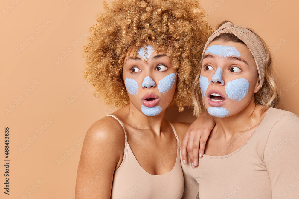 Horizontal shot of shocked amazed women stare away gasp from surprise cannot believe in something terrifying apply beauty mask wear casual clothes isolated over beige background blank space. Horizontal shot of shocked amazed women stare away gasp from surprise cannot believe in something terrifying apply beauty mask wear casual clothes isolated over beige background blank space.