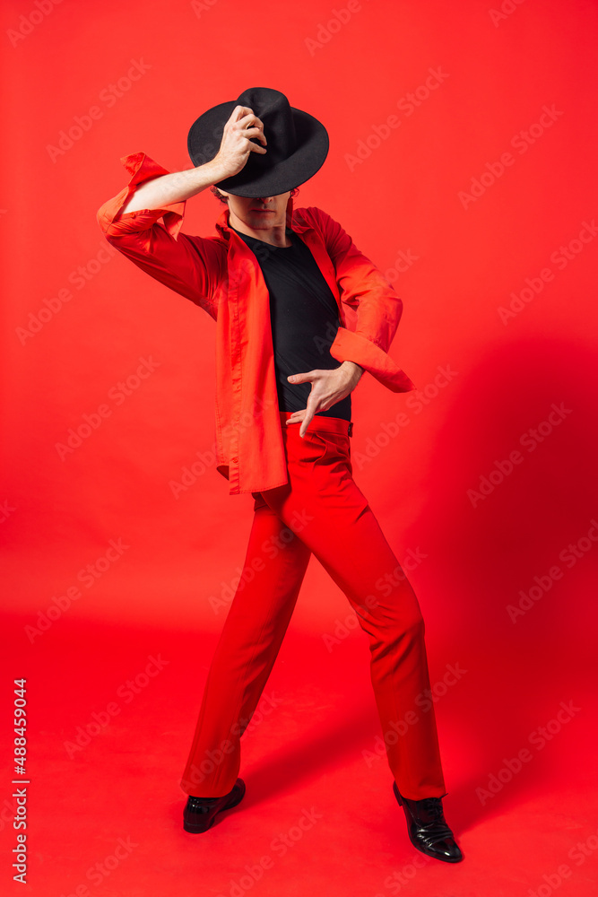 Tall handsome man dressed in red shirt and black hat posing on the red background