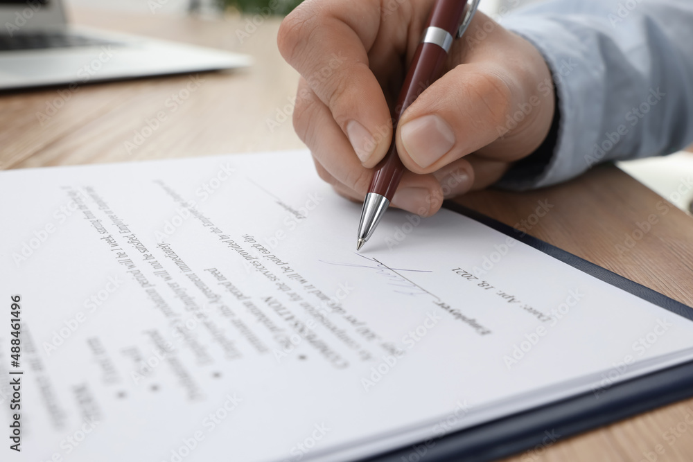 Man signing contract at wooden table, closeup Man signing contract at wooden table, closeup