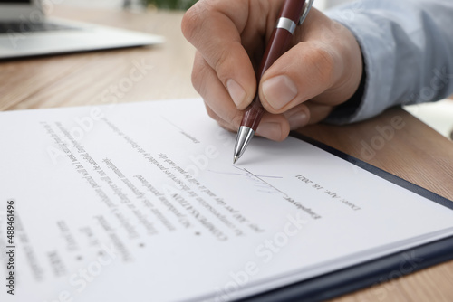Man signing contract at wooden table, closeup