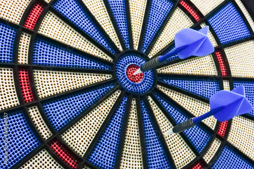 Darts is a sport in which small arrows/darts are thrown at a circular dartboard fixed to a wall. One dart succeeded to hit bulls-eye,centre of the board. The other failed. success story. Conceptual.