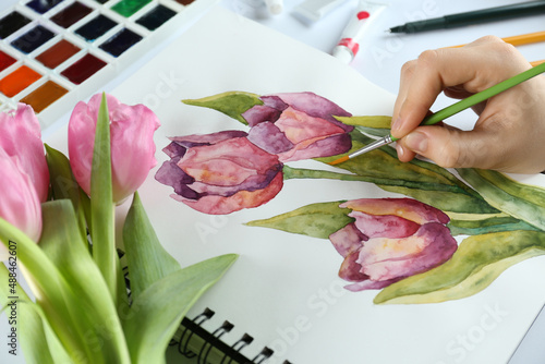 Woman painting tulips in sketchbook at white table, closeup #488462607