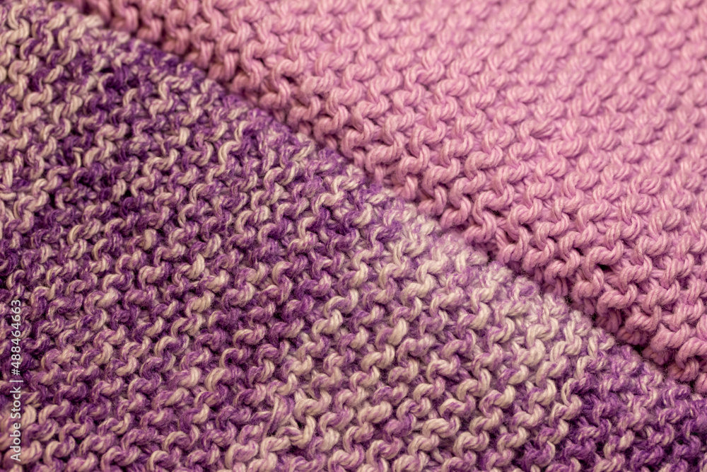 Macro abstract texture background of hand-knitted yarn wash cloths in a simple garter stitch, in varying shades of purple, pink and white