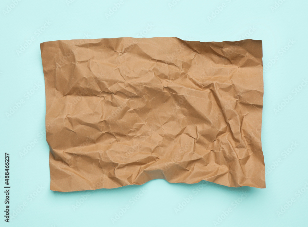 Sheet of crumpled brown paper on light blue background, top view