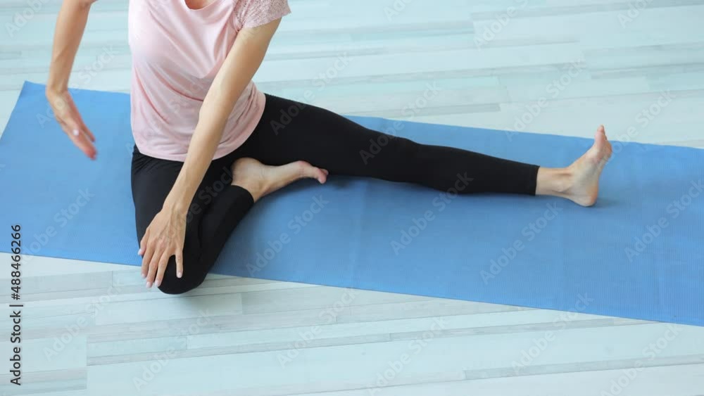 Young woman doing body stretching and sitting on floor in apartment room spbi. 4k video Closeup view Caucasian female stretches legs, arms and sits on mat, does exercise or yoga pose in light interior Young woman doing body stretching and sitting on floor in apartment room spbi. 4k video Closeup view Caucasian female stretches legs, arms and sits on mat, does exercise or yoga pose in light interior