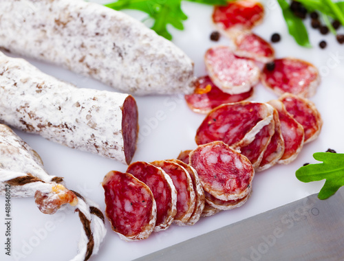 Sliced spanish sausage fuet on a ceramic plate with kitchen knife on a wooden background