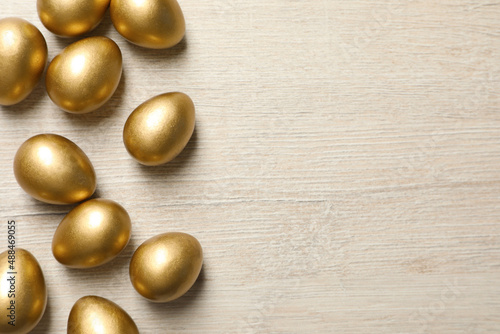 Many golden eggs on white wooden table, flat lay. Space for text