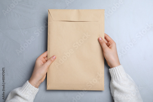 Woman with kraft paper envelope at grey table, top view