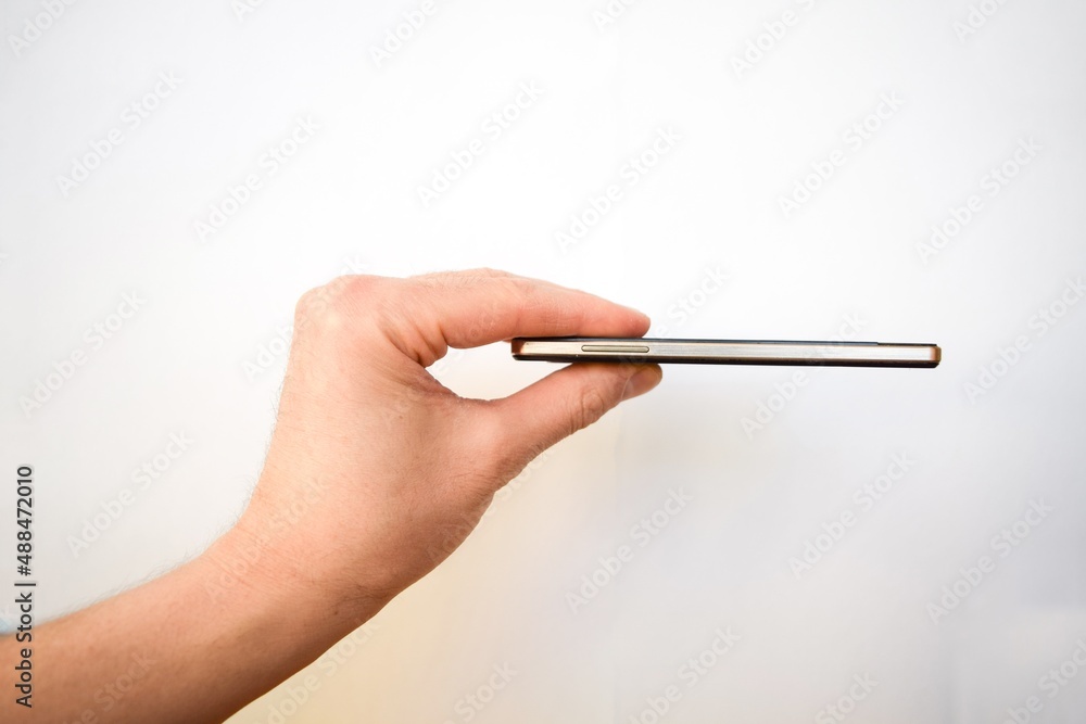 A man's hand holds a thin phone with his fingers on a white background A man's hand holds a thin phone with his fingers on a white background