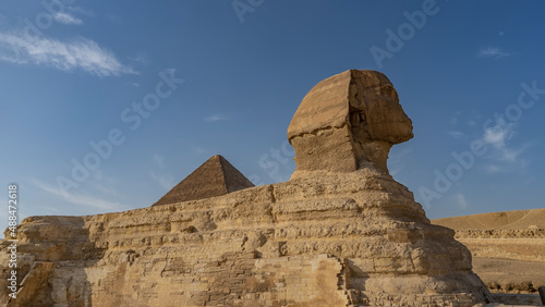 Sculpture of the Great Sphinx. Close-up. Profile view. The top of the pyramid is visible. The background is blue sky. Egypt. Giza
