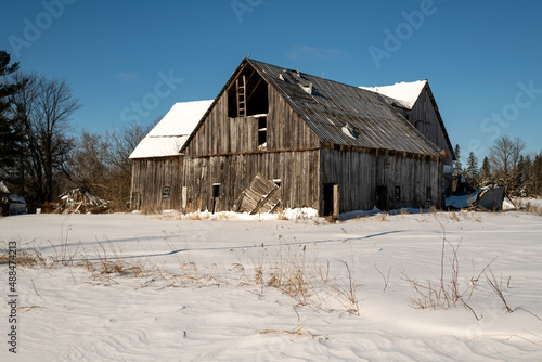 An aging wooden pole barn slowly collapsing. Shot on a sunny day in winter with fresh snow and blue sky.