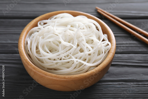 Bowl of tasty cooked rice noodles and chopsticks on black wooden table, closeup