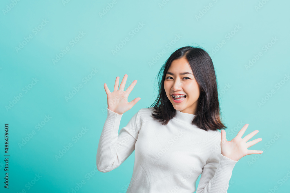 Fototapeta premium Young beautiful Asian woman cheerful smiling makeup showing open hands, Portrait happy female shocked she shows palms, studio shot isolated on a blue background