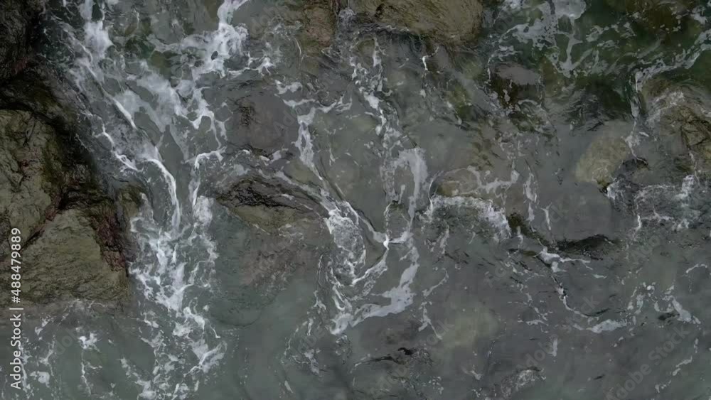 Waves gently rolling and crashing over rocks on the ocean shoreline. Aerial top down view Waves gently rolling and crashing over rocks on the ocean shoreline. Aerial top down view