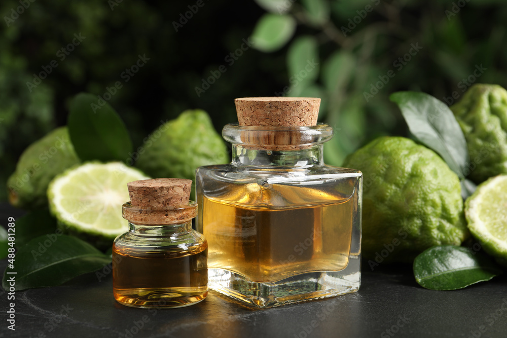 Glass bottles of bergamot essential oil and fresh fruits on black stone table Glass bottles of bergamot essential oil and fresh fruits on black stone table