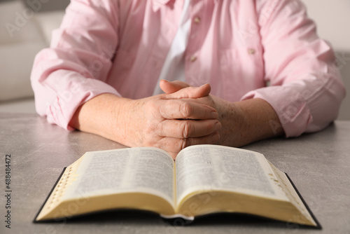 Mature woman with Bible praying at grey table indoors, closeup
