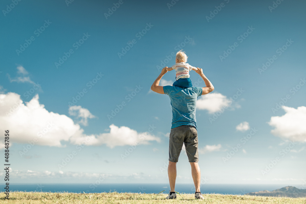 Father caring his son on shoulders facing a beautiful nature view. 