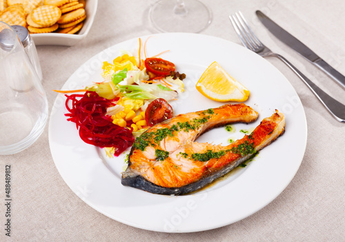 Salmon steak with corn, lettuce, beetroot salad served on plate with piece of lemon.