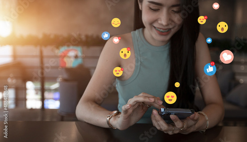 A beautiful blogger, businesswoman, vlogger or influencer gets emoji and emoticon reactions on her mobile smart device while posting. Sharing or recording videos on social media and marketing © Urupong