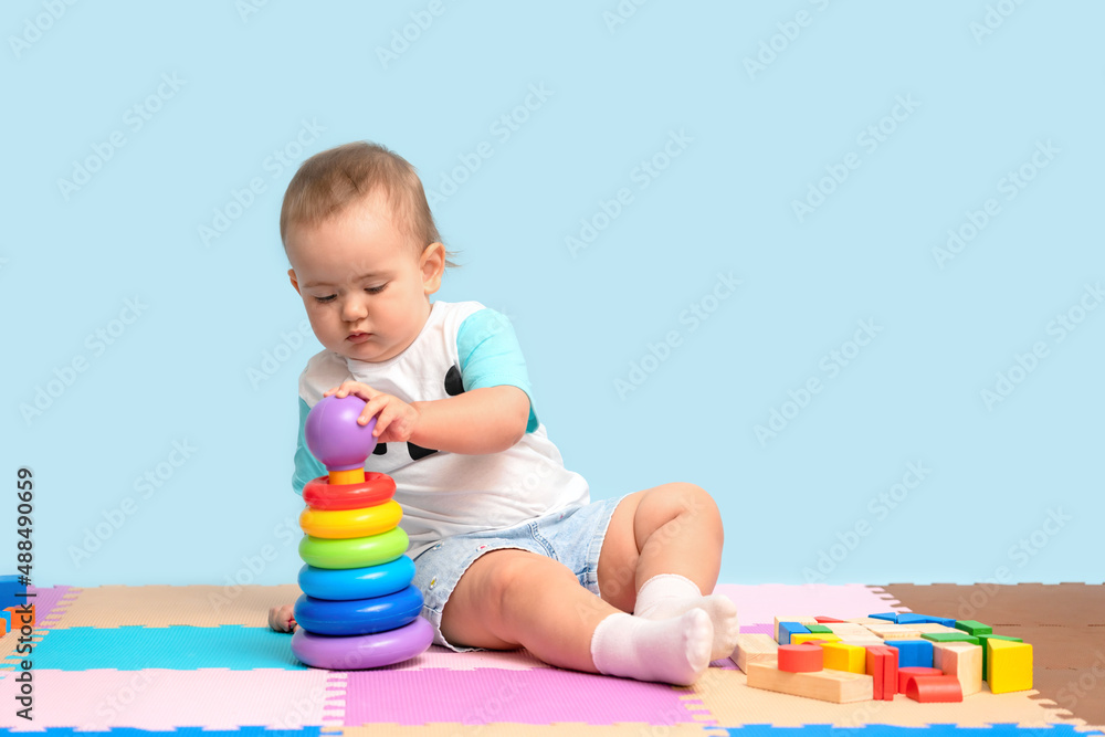A kid of 15-23 months is sitting and assembling a pyramid toy, putting colorful rings on the plastic base of the tower. A kid of 15-23 months is sitting and assembling a pyramid toy, putting colorful rings on the plastic base of the tower.