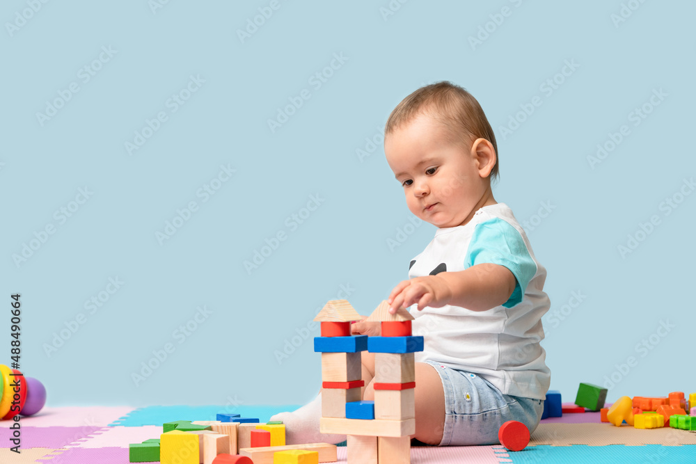Toddler 12-17 months old builds a tower of wooden cubes sitting on the floor in the playroom. Copy space Toddler 12-17 months old builds a tower of wooden cubes sitting on the floor in the playroom. Copy space