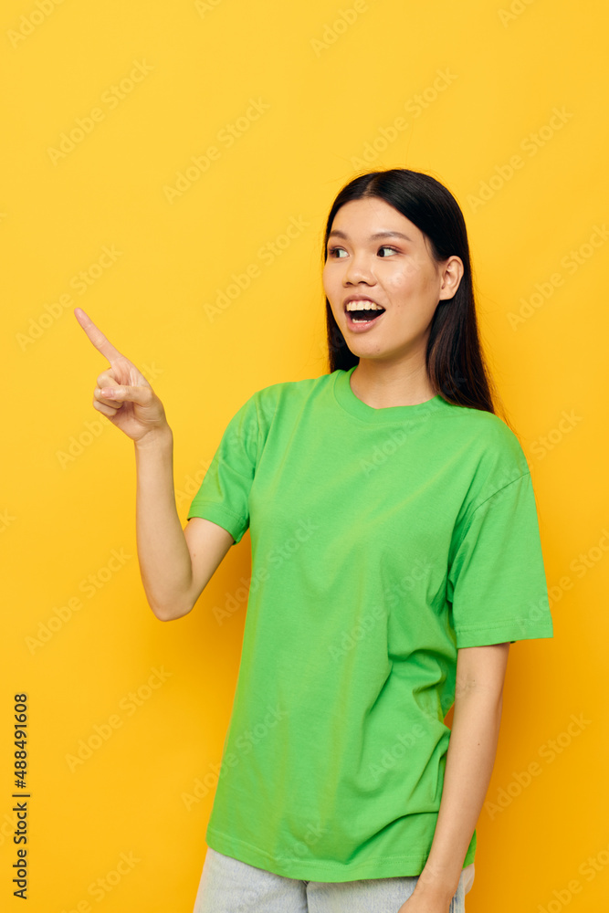 woman with Asian appearance in green t-shirts gestures with his hands emotions yellow background unaltered woman with Asian appearance in green t-shirts gestures with his hands emotions yellow background unaltered
