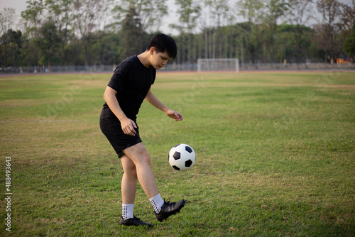 Sports and recreation concept a male soccer player wearing black t-shirt and pants practicing kicking the ball in the grassy field © Pichsakul