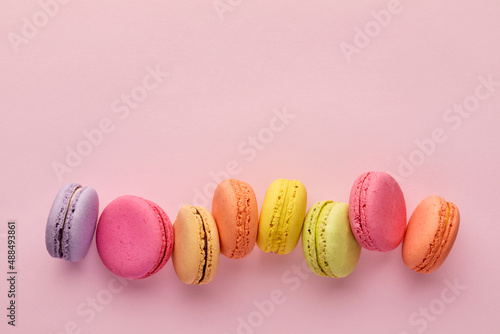 Colorful delicious French dessert macaron or macaroons in a row on pink background.