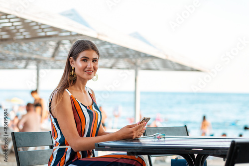 Suumer vacation. A smiling woman sits in a cafe and uses a mobile phone. Concept of communication and social networks