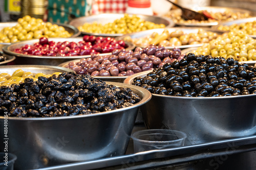 A stall selling various types of domestic olives by weight in the market.