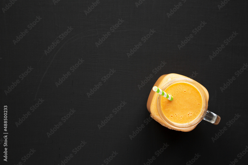 Homemade Carrot Clementine Banana Smoothie in a Glass Jar on a black background; top view. Flat lay, overhead, from above. Copy space.