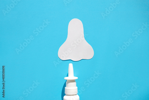 Paper silhouette of a nose and a can of spray on a blue background. Concept against allergic nasal congestion.