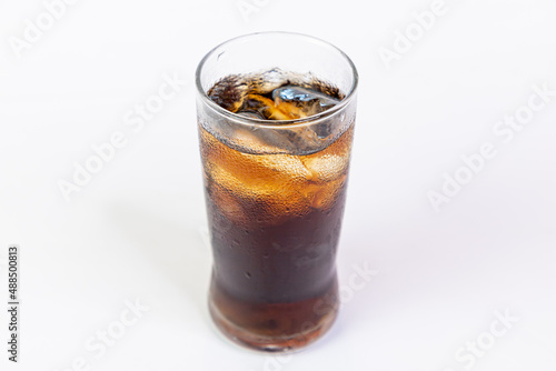 Coca-Cola flavored black soft drink with ice in a clear glass on a white background.