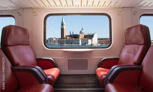 Train window with Venice landscape and empty seats.