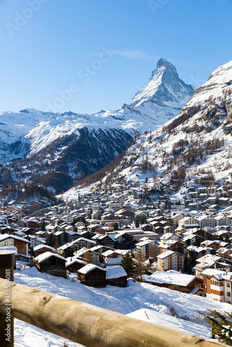 Mountainous landscape overlooking small township of Zermatt in snow covered Swiss Alps on sunny winter day and high pyramidal rock of Matterhorn in background