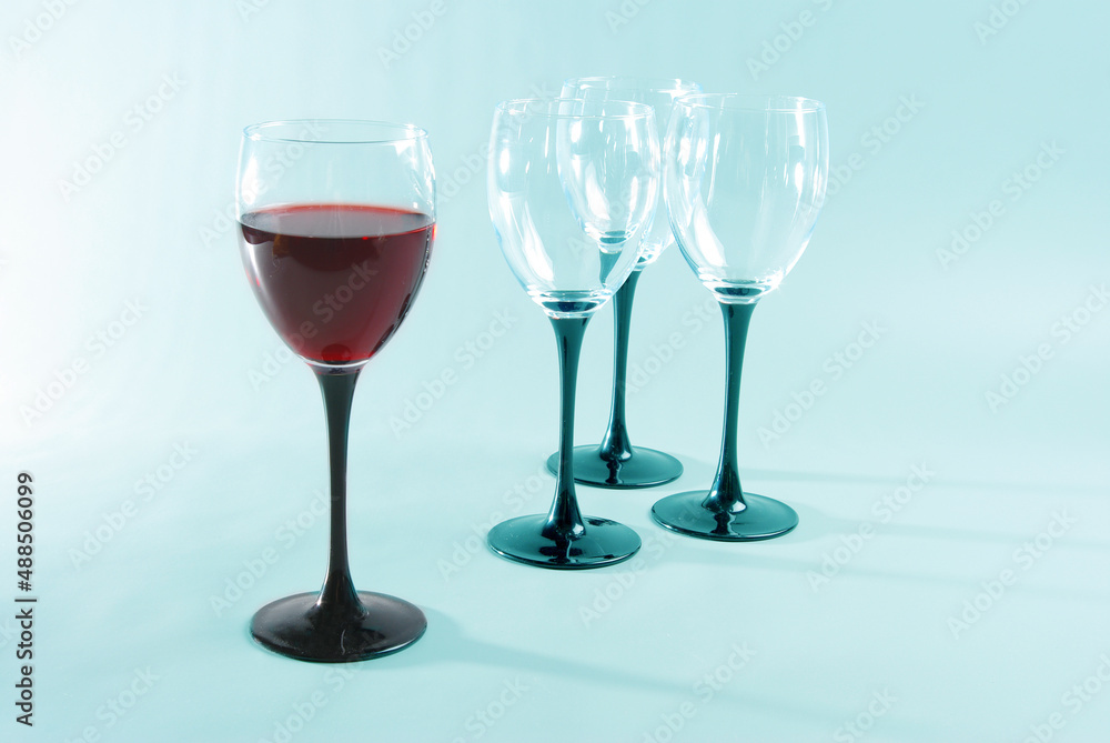 Obraz premium A glass of red wine and three empty glasses on a bluish background.