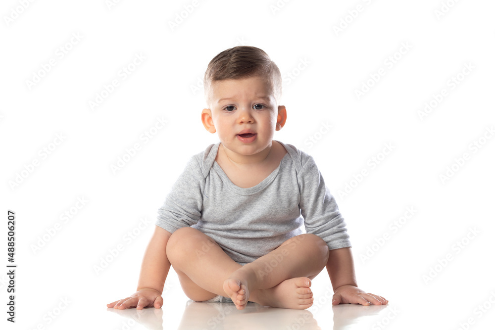 Little smiling baby in bodysuit sitting barefoot on the floor