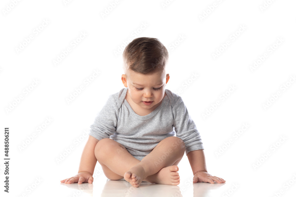 Little smiling baby in bodysuit sitting barefoot on the floor Little smiling baby in bodysuit sitting barefoot on the floor