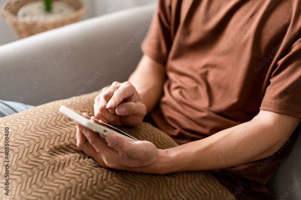 Technology Concept The man sitting next to a pot of plant, putting a small pillow on his lap, and checking something on his smartphone Technology Concept The man sitting next to a pot of plant, putting a small pillow on his lap, and checking something on his smartphone
